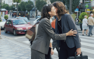 Deux femmes se saluent en se faisant la bise dans une rue de ville, lors d’un échange du quotidien.