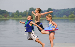 3 enfants sautent dans un lac en été, le visage souriant;