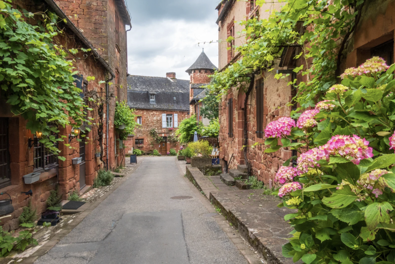 Facade de pierres rouges, et plantes vertes vue dans une rue du village de Collonges-la-Rouge – Corrèze