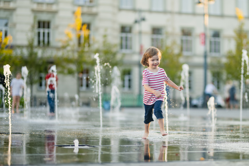 une petite fille qui joue avec des fontaines à eau en centre ville