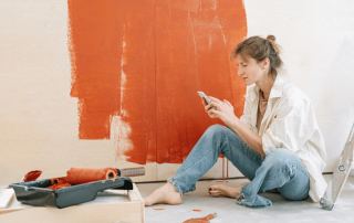femme qui est entrain de faire des travaux et repeindre un mur en regardant son téléphone