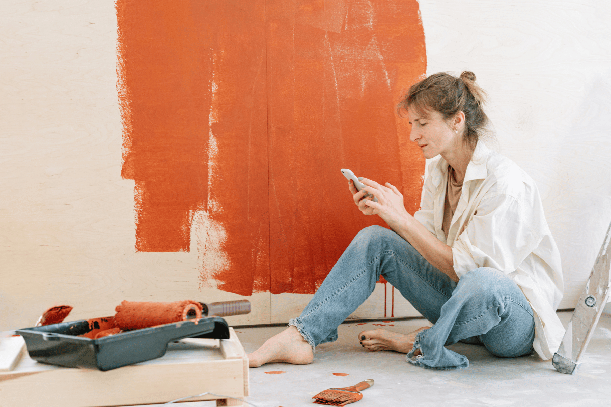 femme qui est entrain de faire des travaux et repeindre un mur en regardant son téléphone